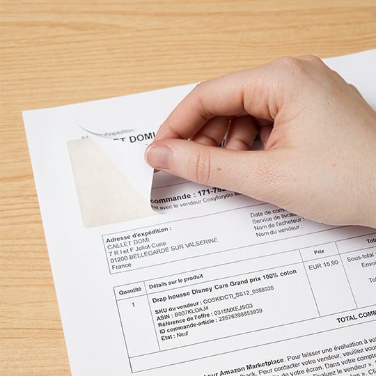 main en train de décoller une étiquette autocollante intégrée sur un document