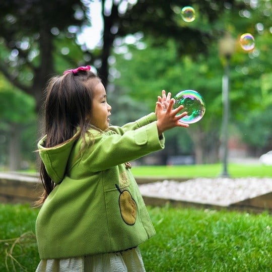 Enfant de 2 ans qui fait des bulles de savons dans l'herbe