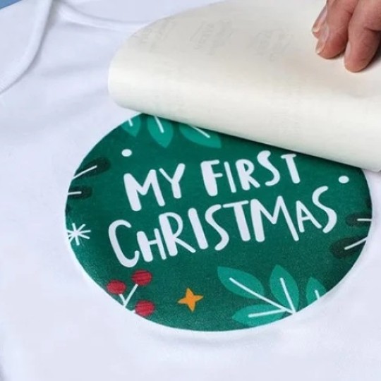Main en train de réaliser un transfert textile sur t-shirt blanc avec un design de Noël