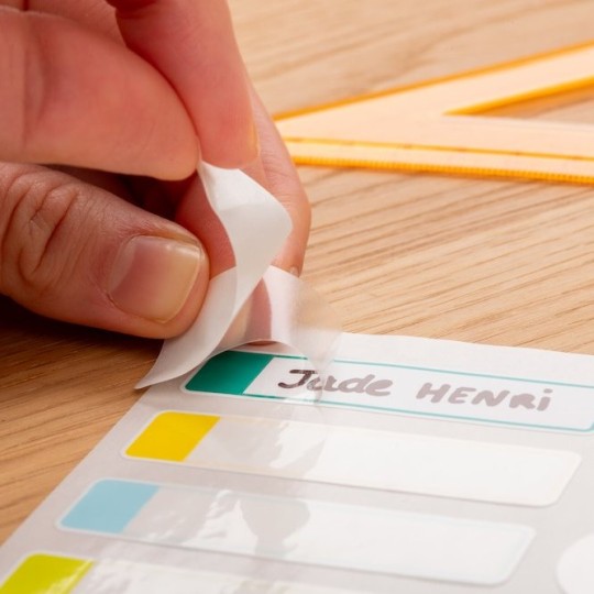 Main qui soulève le film de protection transparent de l'étiquette plastifiée pour le matériel scolaire