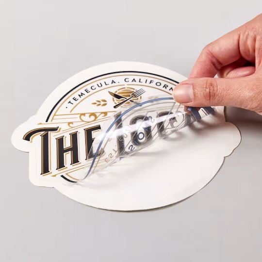 Impression d'étiquettes et stickers transparents doigt soulevant un sticker transparent de son support