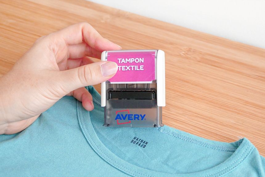 Marquage d'un t-shirt bleu au prénom de l'enfant avec un tampon textile