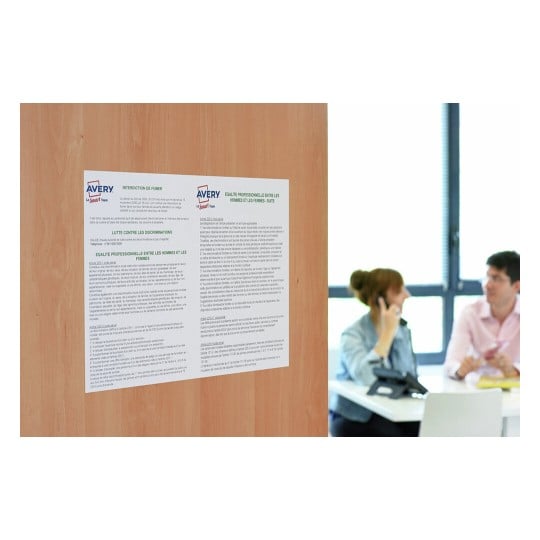 L'image montre des affiches accrochées sur un mur, abordant des thèmes tels que l'interdiction de fumer et l'égalité professionnelle entre les hommes et les femmes. Au fond, deux personnes sont assises à une table, l'une dans un appel téléphonique.