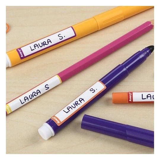 L'image montre plusieurs stylos colorés étiquetés avec le nom 'Laura S.' sur un fond en bois.
