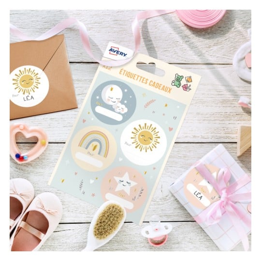 Cette image montre des étiquettes cadeaux colorées avec des illustrations joyeuses, un enveloppe en papier kraft, une petite boîte cadeau et d'autres accessoires sur une surface en bois.