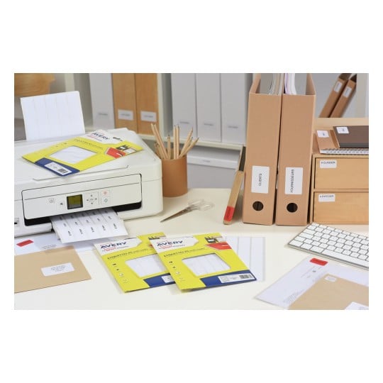 Cette image montre un bureau organisé avec une imprimante, des étiquettes Avery, des dossiers, des enveloppes et un clavier.