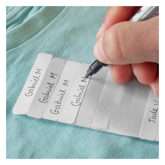 Une personne écrivant des noms sur des étiquettes en papier blanches, posées sur un tissu bleu.
