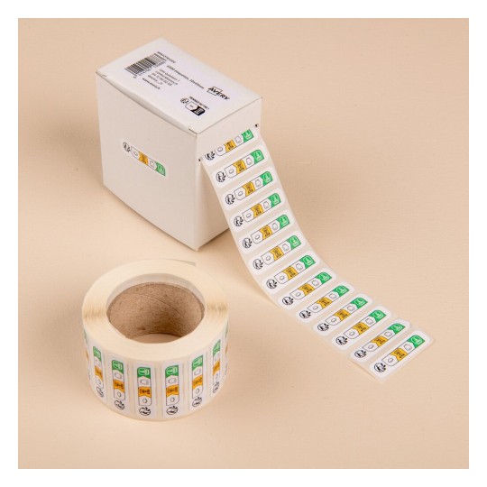 L'image montre une boîte contenant des rouleaux d'étiquettes autocollantes, avec des sections de couleurs verte, jaune et rouge, probablement utilisées pour l'organisation ou l'étiquetage.