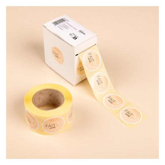 L'image montre une boîte de rouleaux d'étiquettes autocollantes avec des cœurs et le mot 'FAIT', sur un fond beige.