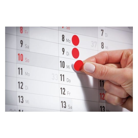 Une personne met un autocollant rouge sur un calendrier, indiquant une date. Les jours de la semaine sont affichés, avec le 10 marqué.