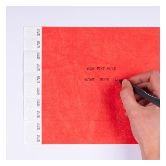 L'image montre une main écrivant sur un papier rouge avec des lignes et des étiquettes blanches sur le côté gauche. Les mots 'YOUR TEXT HERE' et 'VOTRE TEXTE ICI' sont visibles.