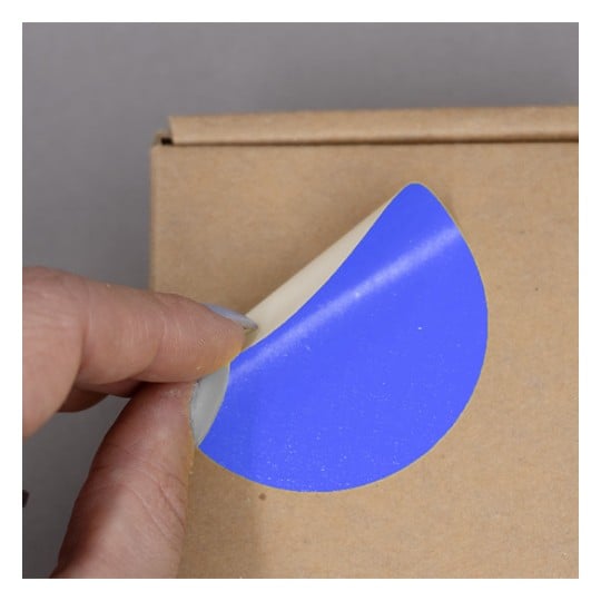 Une main tenant un autocollant bleu qui se décolle d'un carton.