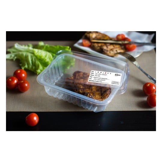 L'image montre un plat en plastique transparent contenant de la viande marinée, entouré de tomates cerises et de feuilles de laitue sur une table.