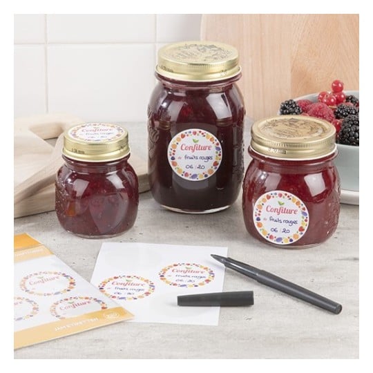 Des bocaux de confiture de fruits rouges sont présentés sur une table, accompagnés d'étiquettes et d'un marqueur.