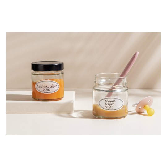 L'image montre deux pots en verre de purée pour bébés, un contenant des carottes et de la crème et l'autre de la banane et de la pomme, avec une cuillère rose et une tétine à côté.