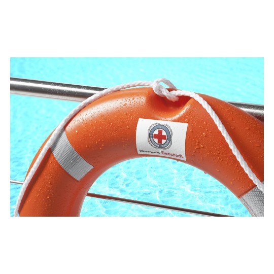 Un bouée de sauvetage orange sur le bord d'une piscine, avec de l'eau bleue en arrière-plan. La bouée est marquée 'Wasserwacht Seestadt'.