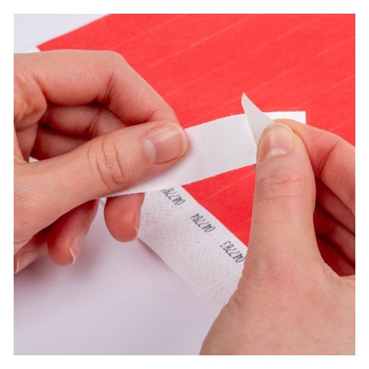 L'image montre une personne qui retire délicatement un morceau de papier adhésif d'une bande, avec un fond rouge.
