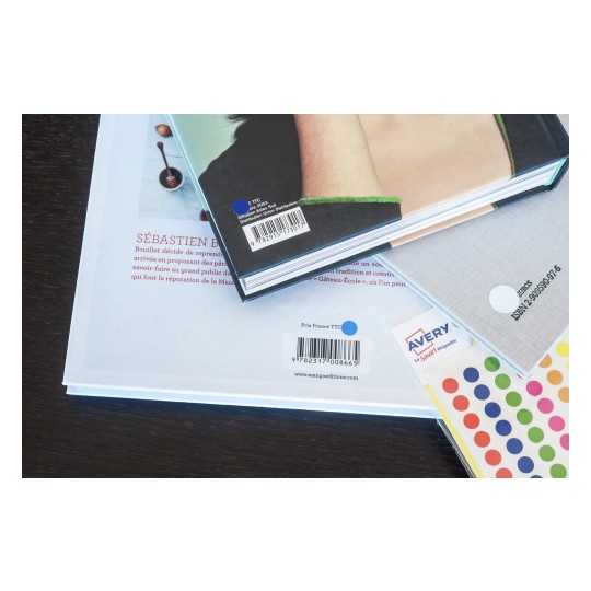 Un affichage de plusieurs livres et étiquettes sur une table en bois. L'un des livres présente un auteur et des informations sur le prix.
