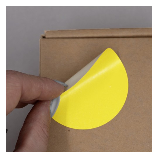 L'image montre une main en train de décoller un autocollant jaune sur un emballage en carton.
