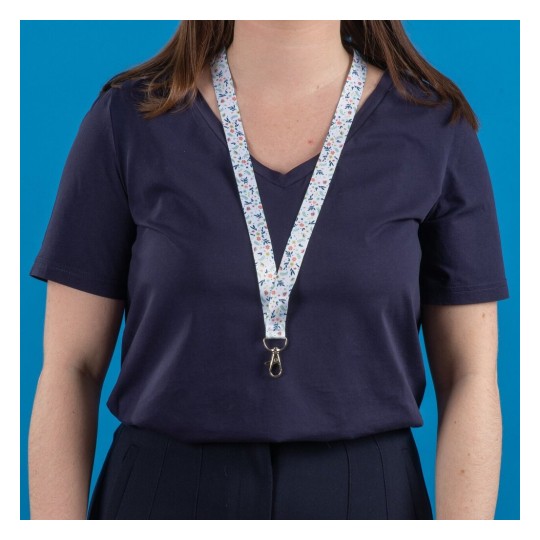 Une personne portant un t-shirt sombre et un lanyard décoré de motifs floraux sur un fond bleu.