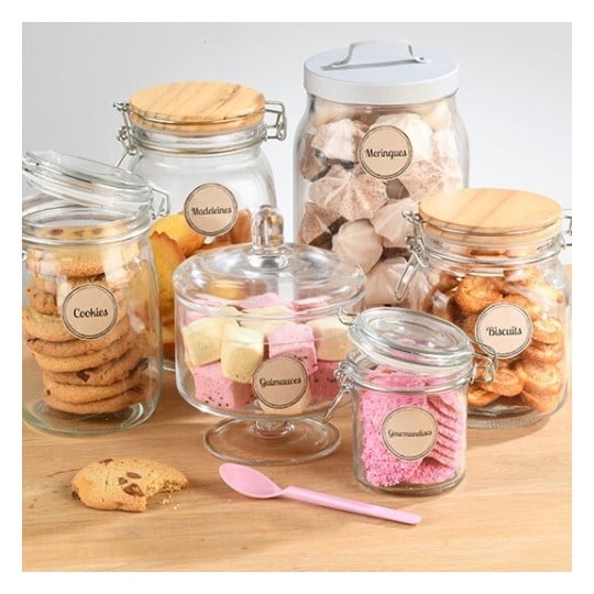 L'image montre plusieurs bocaux en verre remplis de différentes douceurs comme des cookies, madeleines et guimauves, étiquetés avec les noms des sucreries.