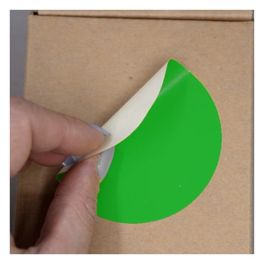 Une main soulève un autocollant vert sur un fond de boîte en carton.