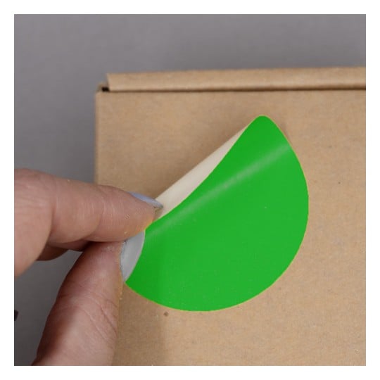 L'image montre une personne qui retire un autocollant vert sur une boîte en carton.