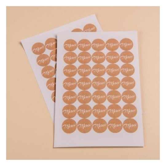 Deux feuilles autocollantes contenant des étiquettes circulaires avec le mot 'Merci' imprimé en blanc sur un fond brun.