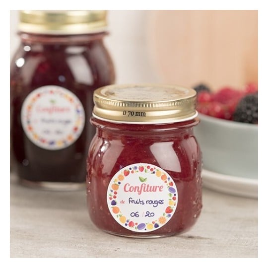 Des pots de confiture de fruits rouges avec des étiquettes sur un fond flou, entourés de baies.