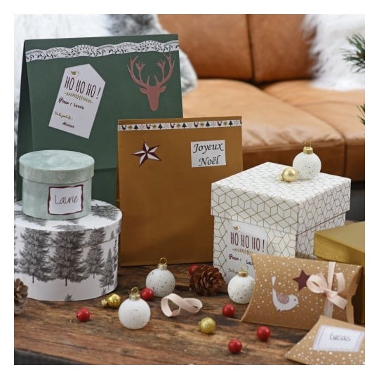 L'image montre des cadeaux et des décorations de Noël, y compris des boîtes emballées, des étiquettes de cadeaux, et des ornements sur une table en bois.