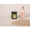 Etiquette règlementaire pour bougie en papier kraft collée sur un contenant vert pour bougie avec des planches d'étiquettes à côté