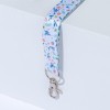 L'image montre un porte-clés ou un cordon décoré de motifs floraux colorés, attaché à un crochet en métal, reposant sur une surface blanche.