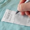 Une personne écrivant des noms sur des étiquettes en papier blanches, posées sur un tissu bleu.