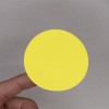 L'image montre un cercle jaune tenue par une main, sur un fond gris.