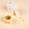 L'image montre une boîte de rouleaux d'étiquettes autocollantes avec des cœurs et le mot 'FAIT', sur un fond beige.