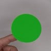 Une main tenant un petit disque circulaire vert sur un fond neutre.