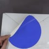 L'image montre une personne tenant un cercle bleu qui semble être une étiquette ou un autocollant, en train d'être décollé d'un carton blanc.