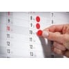 Une personne met un autocollant rouge sur un calendrier, indiquant une date. Les jours de la semaine sont affichés, avec le 10 marqué.