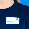 L'image montre une personne portant un t-shirt bleu marine avec un badge d'identification. Le badge indique le nom "Emma Garcia" et le titre "Project Manager".