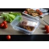 L'image montre un plat en plastique transparent contenant de la viande marinée, entouré de tomates cerises et de feuilles de laitue sur une table.