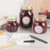Des bocaux de confiture de fruits rouges sont présentés sur une table, accompagnés d'étiquettes et d'un marqueur.