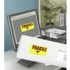 L'image montre un ordinateur de bureau avec un écran affichant un étiquette 'FRAGILE' et un tube ou une boîte avec la même étiquette au premier plan. Le bureau est organisé avec des documents et une plante en arrière-plan.
