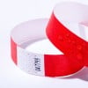 L'image montre un bracelet en papier rouge et blanc, avec des gouttes d'eau sur sa surface. Il semble utilisé pour l'identification ou l'accès à un événement.