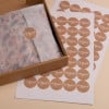 L'image montre une boîte en carton contenant un papier kraft avec une étiquette 'Merci', ainsi que des feuilles de papier décorées de cercles portant le même texte.