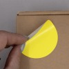 L'image montre une main en train de décoller un autocollant jaune sur un emballage en carton.