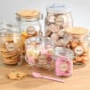 L'image montre plusieurs bocaux en verre remplis de différentes douceurs comme des cookies, madeleines et guimauves, étiquetés avec les noms des sucreries.