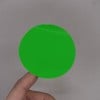 L'image montre un cercle vert brillant tenu par une main contre un fond uniforme.