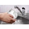 Une personne lave un bocal en verre sous un robinet dans un évier. L'eau coule du robinet sur le bocal.
