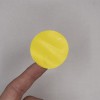 Il s'agit d'un cercle jaune sur un doigt, sur un fond gris. Le cercle semble en matériau lisse avec une texture légère.