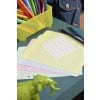 L'image montre un bureau avec des feuilles de papier colorées, des marqueurs dans un récipient jaune, et une petite figurine d'éléphant verte.